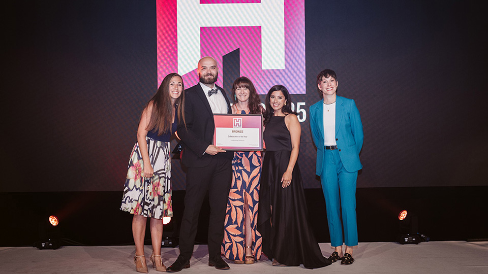 Five people standing together on a stage; one in the center holds a framed certificate.